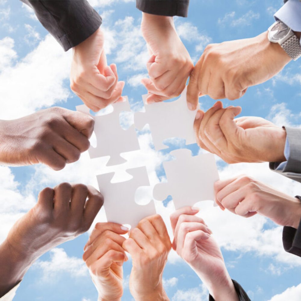 Directly below shot of multiethnic business people assembling jigsaw puzzle against sky